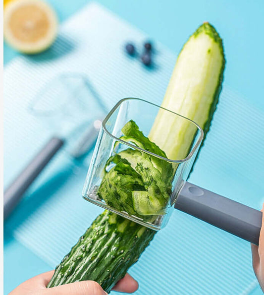 Creative stainless steel peeler in use, slicing cucumber on a blue countertop, showcasing its efficiency for kitchen tasks.